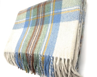 May include: A folded, fringed blanket with a classic plaid pattern. The blanket features a cream-colored base with blue, green, brown, and yellow stripes. The fringe is a light gray color. This cozy blanket is perfect for adding warmth and style to any space.