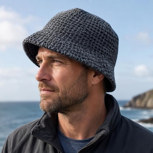 May include: A charcoal gray bucket hat with a textured waffle-knit pattern. The hat features a rounded crown and a downward-sloping brim, crafted from a thick, knit fabric that provides a structured yet flexible fit for head coverage.