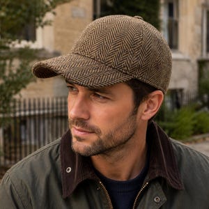 Puede incluir: Una gorra de béisbol marrón y beige con un patrón clásico de espiga. La gorra tiene una corona estructurada y una visera curva, confeccionada con una tela texturizada que muestra un diseño tejido distintivo en toda la superficie exterior.