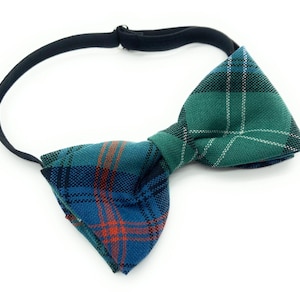 May include: A tartan bow tie with a black elastic strap. The bow tie displays a mix of green, blue, and orange plaid patterns. A smart accessory for formal or casual occasions.