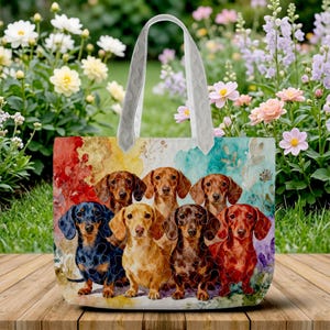 Può includere: Una borsa tote con un design di diversi cani bassotto in vari colori. La borsa ha un manico trapuntato bianco e uno sfondo colorato con accenti floreali. La borsa è appoggiata su una superficie di legno.