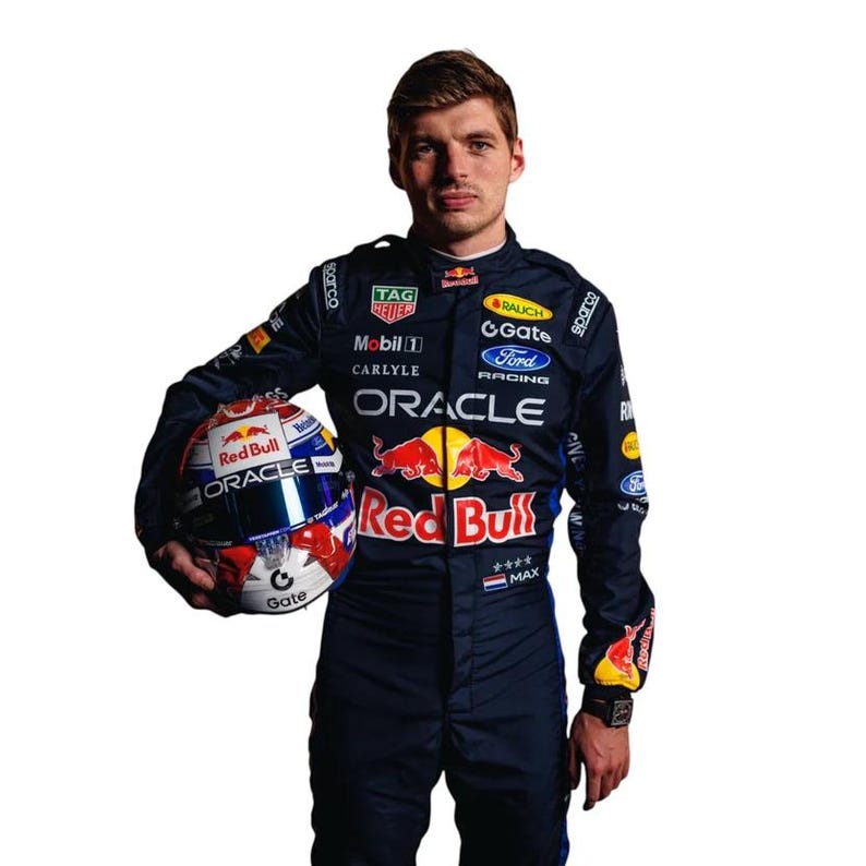 May include: A person wearing a dark blue racing suit and holding a Red Bull racing helmet. The helmet is white, red, and blue with the Oracle logo. The suit has sponsor logos including Oracle, Ford, and Red Bull.