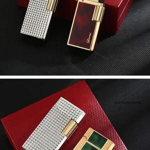 May include: An assortment of luxury lighters in various designs. One lighter features a silver, textured surface, while others have gold accents and colored panels. The lighters are displayed on a red box, with the brand name "Derui" visible.