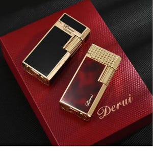 May include: Two rectangular lighters with gold-colored trim and the word "Derui" printed on them. One lighter has a black surface, and the other has a red marbled surface. They are presented on a red box.