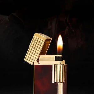 May include: A gold and burgundy lighter with a flame. The lighter is open, revealing a gold patterned top. The text "DERUI" is visible on the lighter. The image also contains the text "At your fingertips, you're the center of attention. Elegant and simple, yet different."