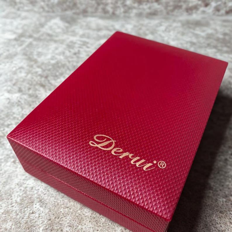 May include: A closed, rectangular red box with a textured surface. The box has a gold-colored script logo that reads "Derui" with a registered trademark symbol.