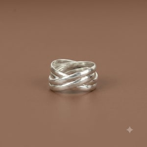 May include: A polished silver ring featuring a multi-band design with several smooth, rounded metal strands that overlap and intertwine to create a continuous, layered structure with a reflective, metallic finish and a uniform, bright silver color.