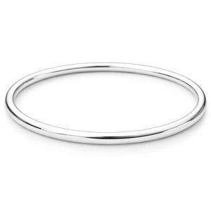 Peut inclure: Un bracelet jonc argenté poli. Le bracelet rond et lisse est une bande pleine de métal brillant, reflétant la lumière. Le bijou est posé sur un fond blanc épuré, soulignant son design minimaliste. Un bijou classique.