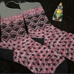 May include: A pair of Cabin Bats socks with a black and pink geometric pattern. The socks are displayed on clear plastic forms. The text "CABIN BATS SOCKS" and "SMALL | MEDIUM | LARGE" are visible. The level is "Confident Beginner".