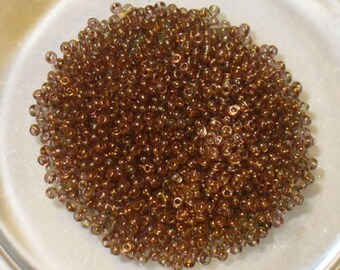May include: A large pile of small, round, iridescent brown glass beads. The beads are translucent and have a slight shimmer to them.