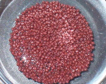 May include: A close-up view of a bowl filled with small, round, red beads. The beads are all the same size and shape, and they are arranged in a random pattern.