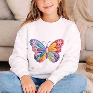Peut inclure: Sweat-shirt blanc orné d'un motif papillon coloré. Le papillon présente un style patchwork avec des nuances de bleu, rose, jaune et orange. Le motif du papillon est centré sur le devant du sweat-shirt.