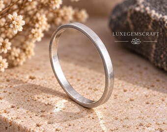 Puede incluir: Un anillo circular delgado de metal plateado con un acabado liso y cepillado. La banda tiene un perfil simple y plano. El texto LUXEGEMSCRAFT es visible en la esquina superior derecha, junto a un icono de flor de loto y líneas horizontales.