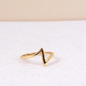 Peut inclure: Une bague dorée avec un motif en zigzag. La bague est faite d'un matériau métallique brillant et est posée sur un fond blanc. Le design de la bague est de style simple et moderne.