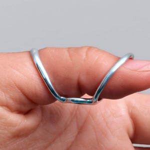 May include: A silver-colored finger splint, designed to support and immobilize the thumb. The splint is made of a thin, curved metal that wraps around the thumb, providing support. The image shows the splint in use.