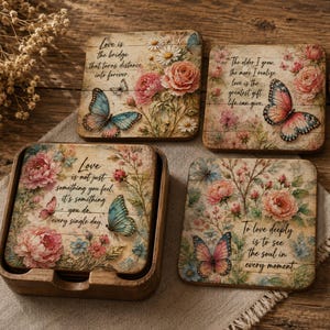 May include: Set of four square wooden coasters with floral and butterfly designs. Each coaster features a different inspirational quote about love. The coasters are displayed in a wooden holder.