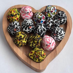 May include: A wooden heart-shaped tray displaying small duck figurines. The ducks are decorated with animal print patterns in black, white, yellow, and pink. The tray is made of light-coloured wood.