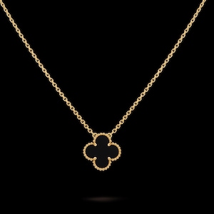 May include: A gold chain necklace featuring a single four-leaf clover pendant. The pendant has a smooth black inlay surrounded by a beaded gold border. The delicate chain connects to the top of the clover motif, creating a simple and elegant piece.