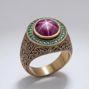 Può includere: Un anello dorato con una grande gemma rotonda, rosso-violacea, con un effetto a stella. La gemma è circondata da piccole pietre verdi. La fascia dell'anello presenta un design ornato e inciso.