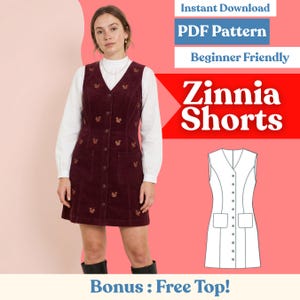 May include: A burgundy corduroy dress with a button-down front, pockets, and squirrel embroidery. The dress is worn over a white blouse. Text on the image reads "Zinnia Shorts", "PDF Pattern", and "Beginner Friendly".