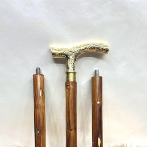 Op de afbeelding: Een houten wandelstok met een goudkleurige handgreep en accenten. De handgreep heeft een sierlijk bloemmotief. De stok bestaat uit drie afneembare delen, met goudkleurige metalen accenten op de houten schacht. De stok wordt gepresenteerd op een lichtbruin oppervlak.