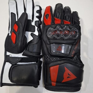 Pu&ograve; includere: Un paio di guanti da moto neri e bianchi con dettagli rossi. I guanti presentano un design protettivo per le nocche e il logo del marchio. I guanti sono in pelle e hanno una chiusura sicura al polso.