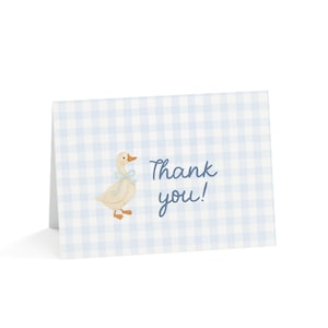 May include: A folded greeting card featuring a light blue gingham design. A cartoon goose with a blue bow is on the left. The words "Thank you!" are written in blue script on the right.