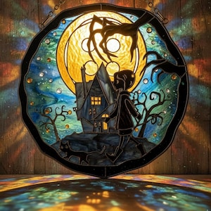 Puede incluir: Panel de vidrieras que representa una escena espeluznante con una luna llena, una casa embrujada y un ni&ntilde;o caminando con un gato negro. La obra de arte tiene un estilo oscuro y caprichoso con un borde negro y una cadena para colgar.