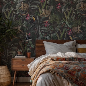 May include: Dark wallpaper featuring a dense jungle pattern with monkeys, toucans, and tropical foliage in shades of green, pink, and brown. The wallpaper serves as a backdrop for a bedroom with a wooden headboard, white bedding, and a patterned throw.