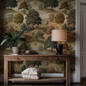 May include: A wooden console table with a lamp, plant, and cushions. The wallpaper depicts a rural scene with trees and horses. The lamp has a dark base and a beige lampshade. The cushions are light-coloured.