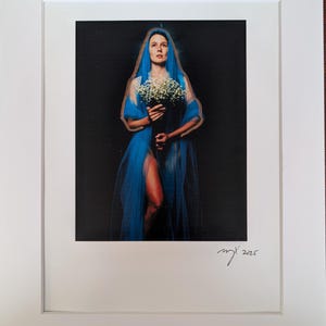 Könnte beinhalten: Gerahmter Kunstdruck mit einer Frau in einem blauen, durchsichtigen Schleier, die einen Strauß weißer Blumen vor schwarzem Hintergrund hält. Der Druck ist signiert und datiert 2025.