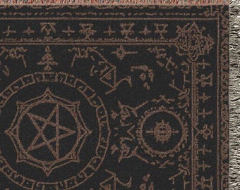 Puede incluir: Manta tejida negra y marrón con un pentagrama y otros símbolos ocultos. La manta rectangular tiene bordes con flecos. El diseño presenta un pentagrama central dentro de un círculo, rodeado de varios símbolos esotéricos.