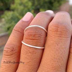 Puede incluir: Primer plano de dos anillos de plata apilados en un dedo. Los anillos son bandas simples. El texto "Daily Wear Jewelry Shop" es visible en la parte inferior izquierda.