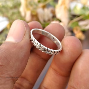 May include: A silver ring with a leaf pattern. The ring is held between fingers, showing the detailed leaf design. The ring is a simple band, suitable for everyday wear. The ring's diameter is approximately 1.7 cm.
