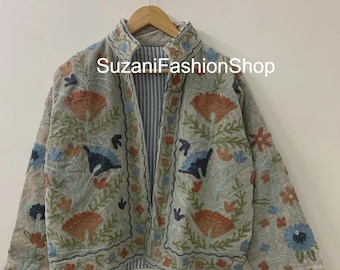 May include: A beige embroidered jacket with a floral design in orange, blue, and green. The jacket has long sleeves and a high collar. The text "SuzaniFashionShop" is visible on the jacket.