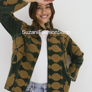 May include: A dark green velvet jacket with a brown embroidered pattern. The jacket has a high collar and long sleeves. The text "SuzaniFashionShop" is visible on the jacket.