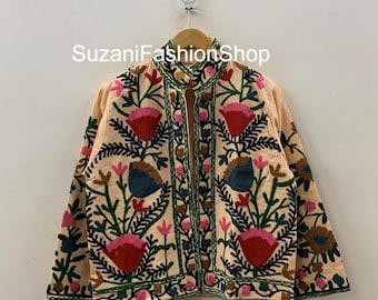 Puede incluir: Chaqueta color melocotón con intrincados bordados florales en rojo, rosa, azul y verde. La chaqueta presenta un cuello alto y está adornada con costuras detalladas, creando un diseño vibrante y artístico. El texto "SuzaniFashionShop" es visible.