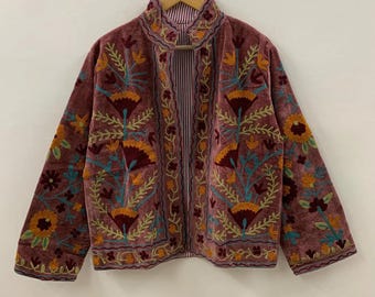 以下が含まれることがあります： オレンジ、黄色、ティール色の花柄刺繍が施された、モーヴ色のベルベットジャケット。 ジャケットはハイカラーと長袖です。 内側の裏地はストライプ柄です。