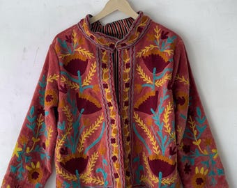 May include: A coral-colored jacket with intricate floral embroidery in shades of burgundy, yellow, and teal. The jacket features a mandarin collar and long sleeves. The text "SuzaniFashionShop" is visible at the top.