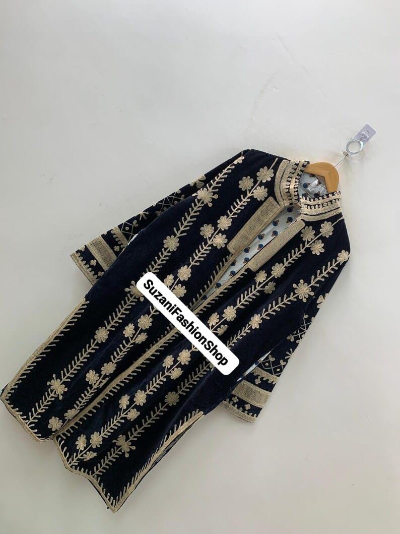 May include: A navy blue velvet coat with detailed gold floral embroidery. The coat has a high collar and gold trim on the edges and sleeves. The text "SuzaniFashionShop" is visible on the front.