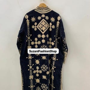 May include: A navy blue embroidered coat with gold floral and geometric patterns. The coat has a high collar and is hanging on a wooden hanger. The text "SuzaniFashionShop" is visible on the coat.