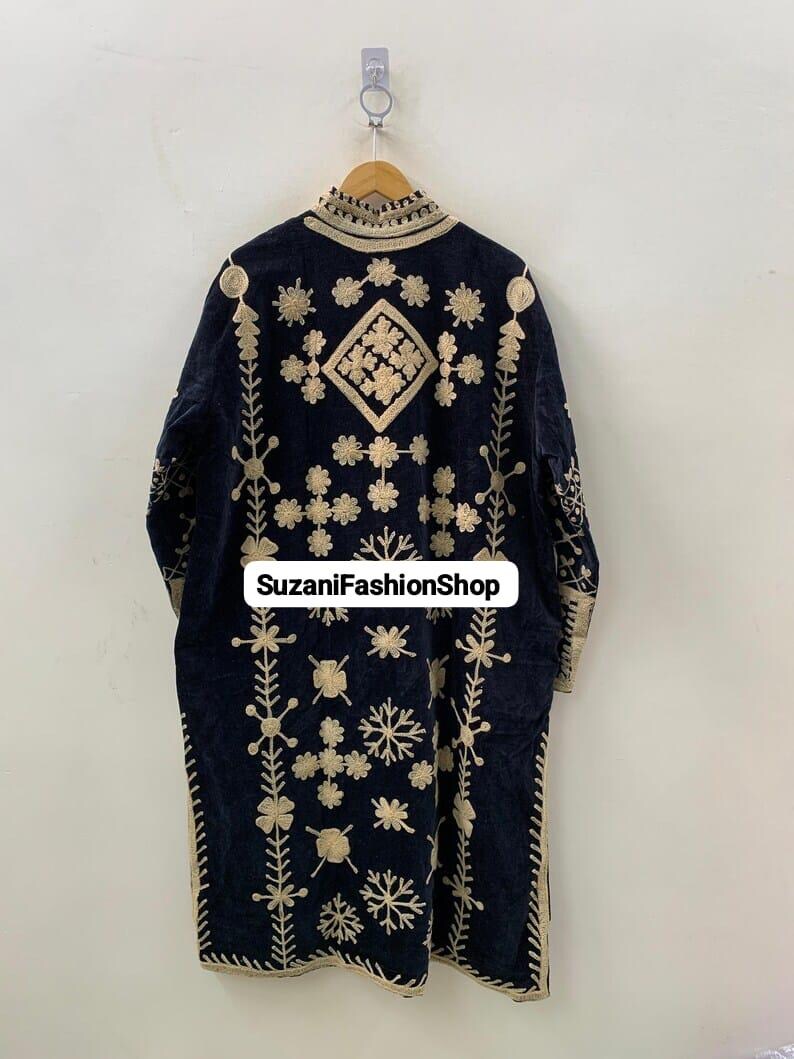 May include: A navy blue embroidered coat with gold floral and geometric patterns. The coat has a high collar and is hanging on a wooden hanger. The text "SuzaniFashionShop" is visible on the coat.
