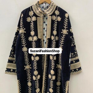 May include: A navy blue velvet coat with gold floral embroidery. The coat has a high collar and is open at the front, showing a patterned lining. The text "SuzaniFashionShop" is visible. The coat is a long style.