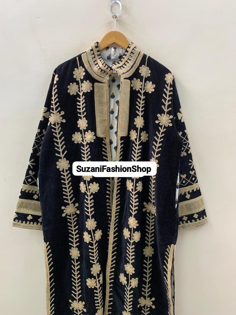 May include: A navy blue velvet coat with gold floral embroidery. The coat has a high collar and is open at the front, showing a patterned lining. The text "SuzaniFashionShop" is visible. The coat is a long style.