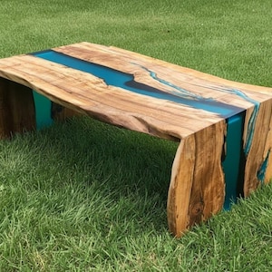 May include: A handcrafted wooden coffee table with a live edge design. The table features a river of turquoise resin flowing through the center. The natural wood grain and turquoise resin create a unique and artistic piece of furniture.