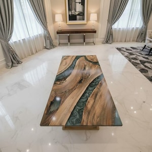 Op de afbeelding: Een rechthoekige houten salontafel met een uniek ontwerp. De tafel heeft een natuurlijk houtnerfpatroon met een rivier van donkerblauwgroene hars in het midden. De tafel wordt ondersteund door een lichtbruine basis. Ongeveer 180 cm lang.