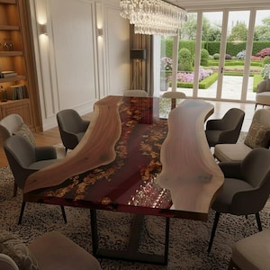 Può includere: Un grande tavolo da pranzo rettangolare con un design a bordo vivo. Il tavolo presenta un centro in resina rosso scuro con accenti dorati ed è circondato da sedie imbottite grigie. La stanza ha un lampadario e una vista su un giardino.