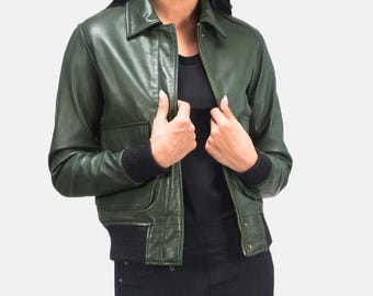 Puede incluir: Chaqueta bomber de cuero verde oscuro con cuello, dos bolsillos delanteros y puños y dobladillo de canalé negros. La chaqueta está desabrochada, revelando una parte superior negra. El modelo lleva pantalones negros.