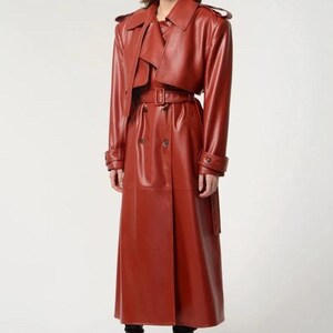May include: A long, rust-coloured leather trench coat. The coat has a double-breasted design, a belted waist, and a notched collar. The sleeves have buttoned cuffs. The coat is worn over a matching top.