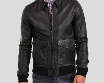 May include: Black leather bomber jacket with a collared neckline, two front pockets, and a ribbed hem and cuffs. The jacket has a zipper closure and is worn over a plaid shirt. A classic outerwear piece.